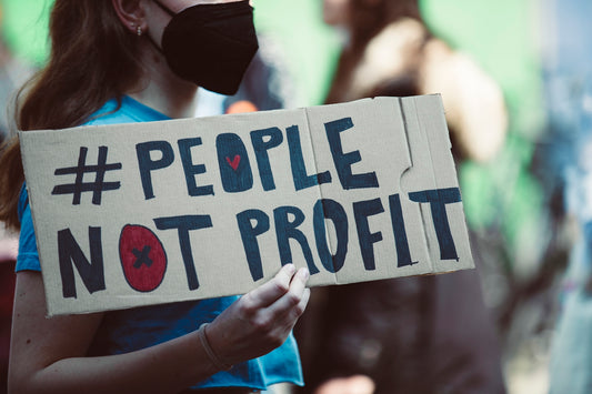 a woman holding a sign that says people not profits
