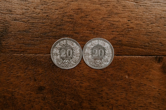 two round silver-colored 20 coins on brown surface