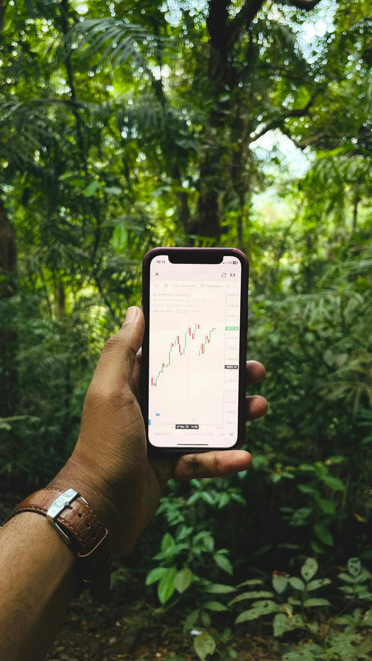 a hand holding a cell phone in front of a forest