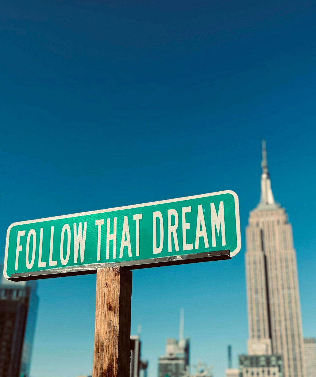 a green and white street sign that says follow that dream